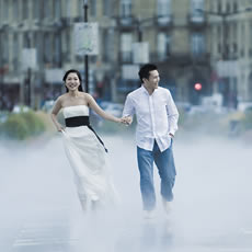 Couple courant main dans la main dans la brume légère du Miroir d'eau de Bordeaux, avec de grands bâtiments en pierre derrière eux