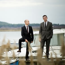 Deux photos côte à côte de deux hommes en costume : l'un sur un ponton au bord de l'eau, l'autre près d'un tas de bûches avec des parapluies