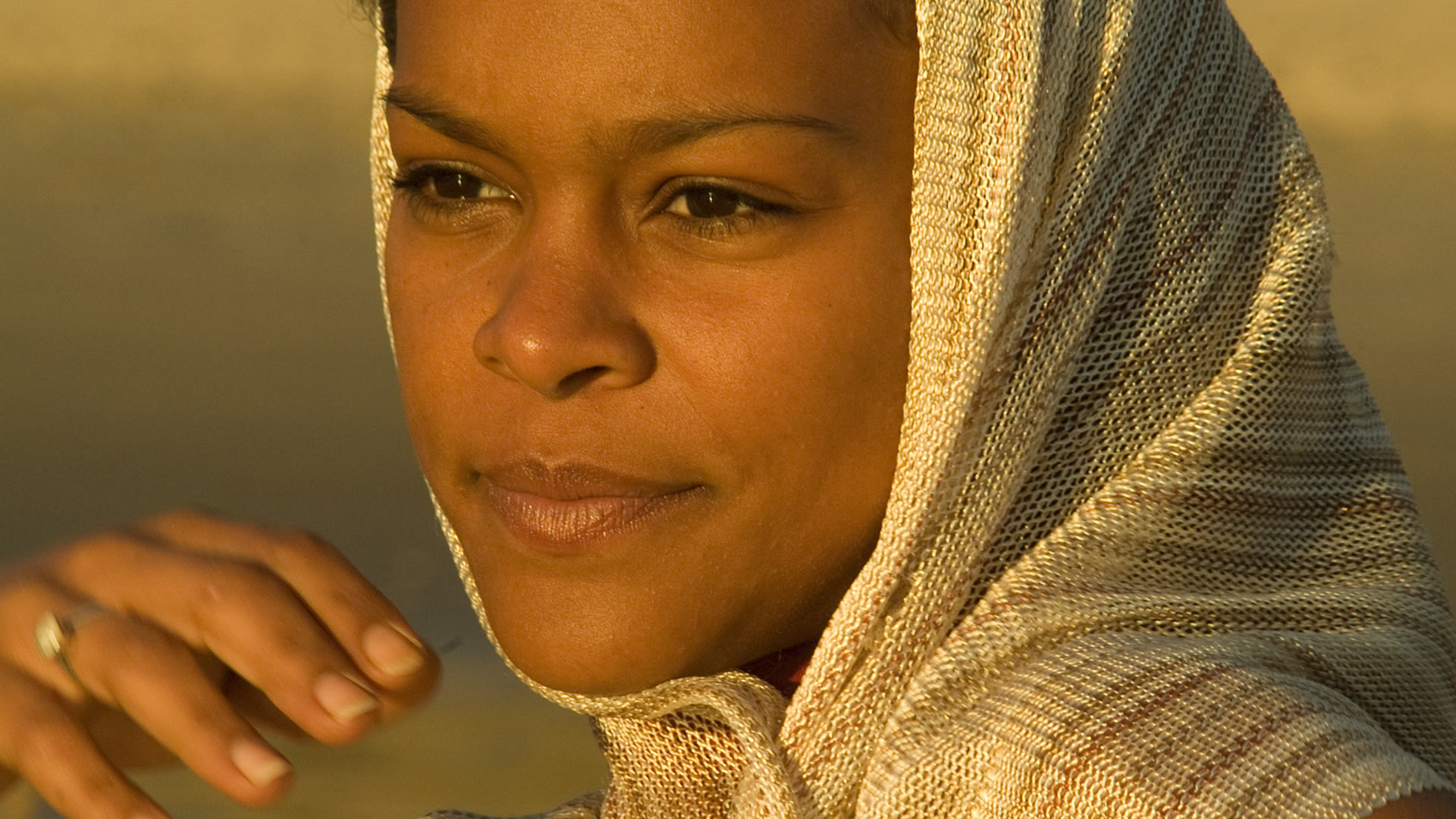 Gros plan d'une femme avec un foulard beige tissé sur la tête, le regard tourné sur le côté, dans la lumière dorée du coucher de soleil
