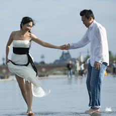 Couple se tenant par la main et marchant pieds nus dans l'eau peu profonde du Miroir d'eau de Bordeaux, elle en robe bustier blanche, lui en chemise blanche et jean