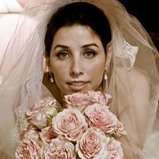 Portrait de mariage en gros plan d'une mariée sous un voile délicat, tenant un bouquet de roses rose pâle.