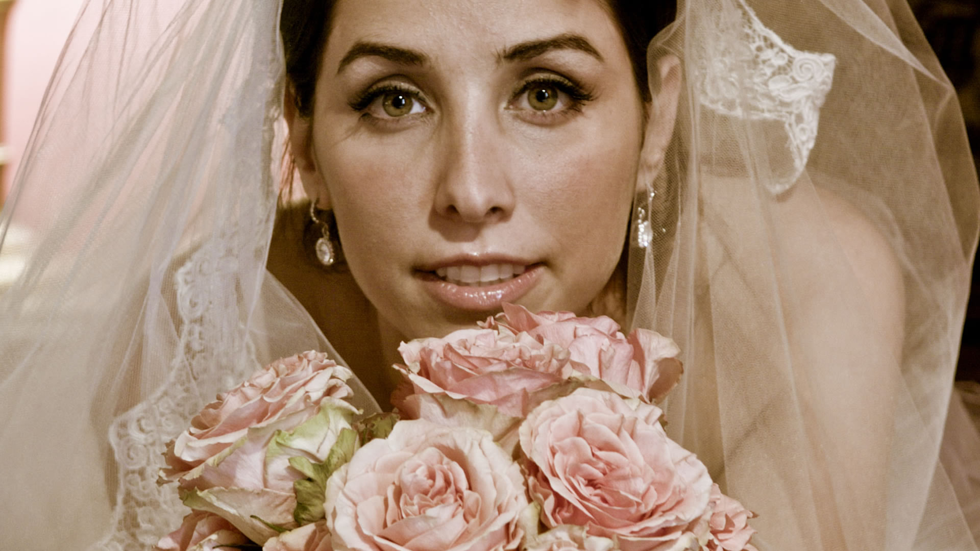 Portrait de mariage en gros plan d'une mariée sous un voile délicat, tenant un bouquet de roses rose pâle.