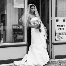 Photographie de mariage en noir et blanc d'une mariée tenant son bouquet devant un café français traditionnel