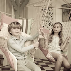 Un garçon et une fille assis dans des fauteuils suspendus rose et crème, dans une pièce lumineuse au style vintage