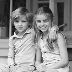 Portrait en noir et blanc d'un garçon et d'une fille souriants, assis côte à côte sur un banc de porche